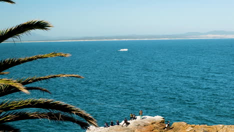 Tourists-in-Hermanus-on-rocky-coastal-lookout-point-watches-a-whale-breach-in-Walker-Bay---whale-season,-South-Africa