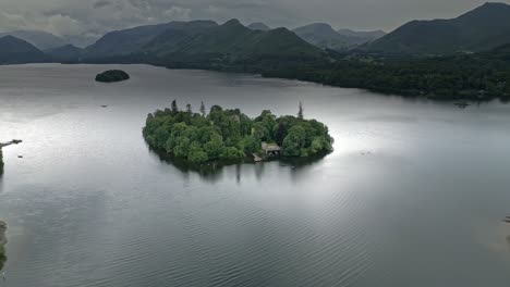 Drone-Aerial-footage-of-a-Island-and-house-on-Derwentwater,-Keswick,-a-calm-lake-with-river-boats-and-a-stormy-sky