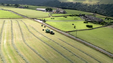 Green-Tractor-harvesting-hay-on-a-rural-landscape-in-Halifax-West-Yorkshire-England,-aerial-view