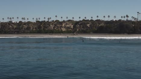 A-beautiful-aerial-drone-shot,-drone-flying-low-over-water-along-the-coast-and-filming-a-couple-of-surfers,-Carlsbad-State-Beach---California