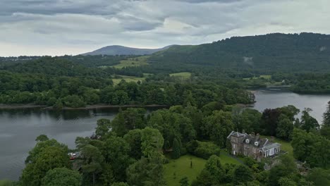 Aerial-video-footage-of-Derwent-Island-on-Derwentwater,-Keswick,-a-calm-lake-with-river-boats-and-a-stormy-sky