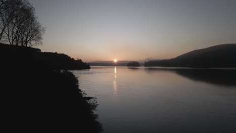 Aufnahme-Eines-Wunderschönen-Sonnenaufgangs-Am-Rande-Des-Sees-Mit-Hügeln-Im-Hintergrund