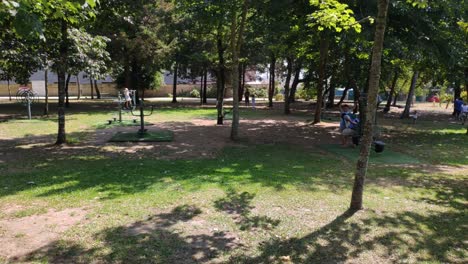 Families-with-children-enjoying-the-games-of-the-public-park-in-the-shade-of-the-trees-on-a-sunny-summer-morning