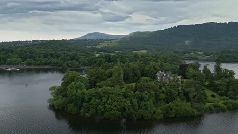 Aerial-footage-of-Derwent-Island-on-Derwentwater,-Keswick,-a-calm-lake-with-river-boats-and-a-stormy-sky