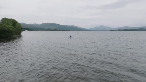 Slow-Tracking-Shot-Of-A-Young-Woman-Paddlebaording-From-The-Shore-Of-Loch-Lomond