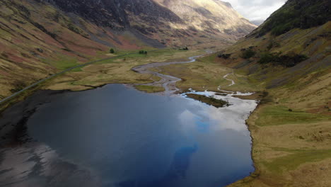 aerial-shot-over-small-lake-and-revealing-the-beautiful-mountains-located-in-the-GLENCOE-HIGHLANDS-VALLEY