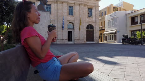 Woman-sitting-cross-legged-on-a-bench-sips-a-coffee-and-enjoys-the-morning-sweetness-in-Chania