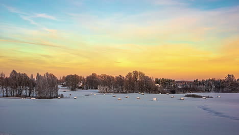 TIme-lapse-wide-shot-of-beautiful-sunset-at-sky-over-winter-landscape-with-snow-covered-hay-bales