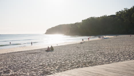 Romantischer,-Malerischer-Strand-Mit-Nachmittagssonne,-Die-Vom-Meer-Reflektiert-Wird,-Und-Menschen-Am-Sandstrand,-4k-Zeitlupe