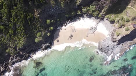 Drone-aerial-top-view-of-waves-breaking-against-a-peaceful-empty-beach-in-Australia