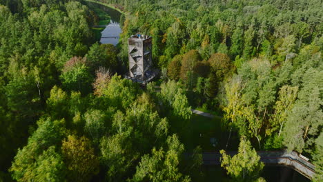 Beautiful-drone-view-flying-through-treetop-walkway-tower-with-people-on-it-between-green-woods-located-in-Anyksciai,-Lithuania,-eastern-Europe