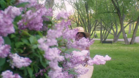 Ethiopian-lady-in-summer-dress-and-hat-stops-to-smell-pink-lilac-flowers
