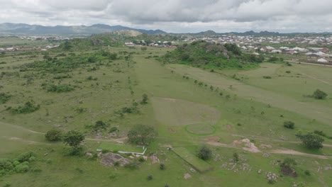 Aerial---golf-course-surrounded-by-rocks-and-a-settlement,-forward-descending