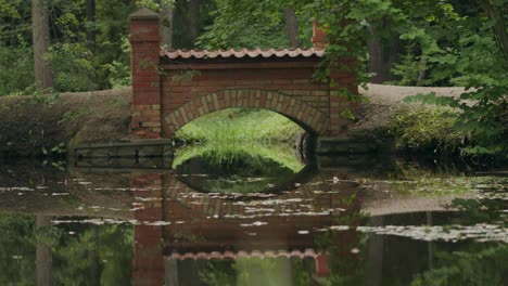 Red-brick-built-arch-footbridge-in-parkland-waterlily-pond-setting