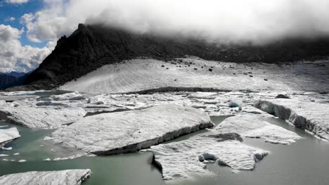Sobrevuelo-Aéreo-Giratorio-Sobre-Icebergs-De-Un-Lago-Glaciar-Que-Se-Derrite-En-Partes-Remotas-De-Los-Alpes-Suizos-En-Un-Día-Soleado