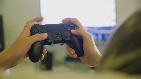 Female-hands-using-black-PS4-dualshock-controller-to-play-game-inside-home-with-TV-in-background