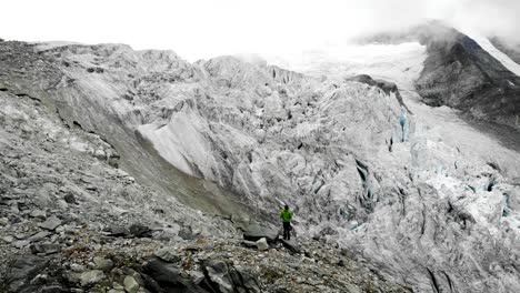 Sobrevuelo-Aéreo-Sobre-Un-Excursionista-Hacia-El-Borde-Del-Glaciar-Moiry-Cerca-De-Grimenz-En-Valais,-Suiza,-Con-Vistas-A-Las-Grietas-Heladas-Y-Los-Picos-Alpinos-Escondidos-En-Las-Nubes