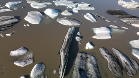 Aerial-background-shot-of-many-broken-ice-pieces-of-a-glacier-on-brown-water,-in-Iceland,-Heinabergsjökul