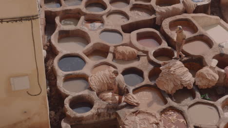Close-up-tannery-workers-placing-leather-pieces-in-massive-baths-of-dye-in-Fes,-Morocco