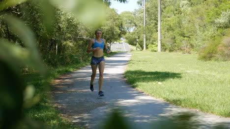 Female-Athlete-Jogging-Through-Green-Park,-Perspective-Through-Trees,-4K-Slow-Motion