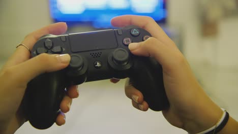 Closeup-of-female-hands-using-black-PS4-dualshock-controller-to-play-game-inside-home-with-TV-in-background