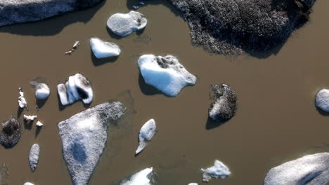 Aerial-zenith-shot-of-many-broken-ice-pieces-of-a-glacier-on-brown-water,-in-Iceland,-Heinabergsjökul