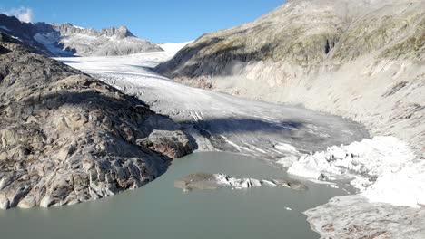 Aerial-view-of-Rhone-glacier-near-Furka-mountain-pass-at-the-border-of-Valais-and-Uri-in-Switzerland-with-a-pan-down-from-the-ice-towards-the-waterfalls-at-the-end-of-the-lake