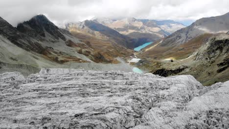 Aerial-flyover-alongside-the-edge-of-the-Moiry-glacier-near-Grimentz-in-Valais,-Switzerland-with-of-the-icy-crevasses,-valley-and-lake-on-a-cloudy-summer-afternoon