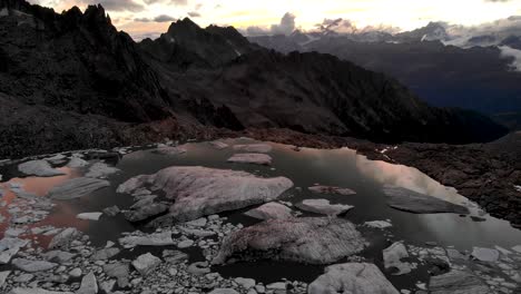Aerial-view-of-a-glacier-lake-full-of-melted-icebergs-in-remote-parts-of-the-Swiss-Alps-during-sunset-with-pan-down