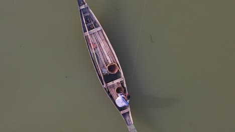 Aerial-Top-Down-View-Of-Lone-Fisherman-On-Traditional-Wooden-Boat-Line-Fishing-On-The-Ichamati-River