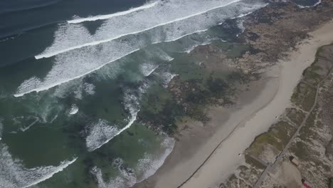 Aerial-shot-of-a-beach-being-washed-off-by-the-waves-of-a-sea