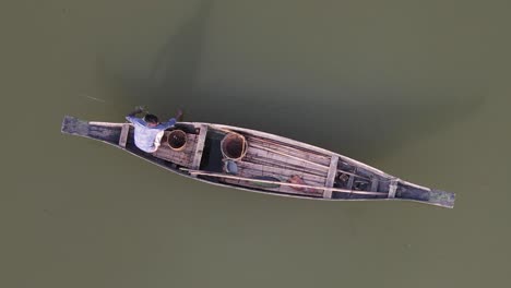 Aerial-Top-Down-View-Of-Lone-Fisherman-On-Traditional-Wooden-Boat-Floating-On-The-Ichamati-River