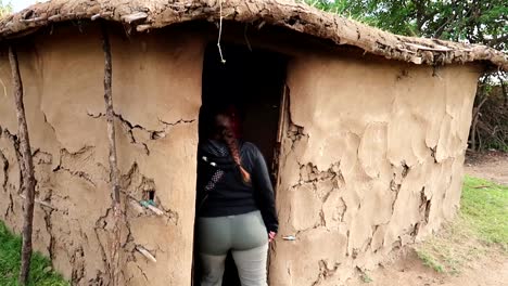 Mujer-Entrando-En-Una-Casa-De-Barro-Hecha-A-Mano-Rural-Masai-Local-Con-Una-Persona-Masai