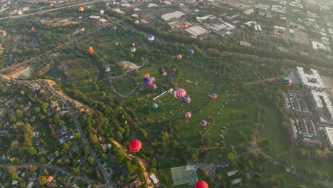 Wide-revealing-drone-shot-of-hot-air-balloons-soaring-above-a-large-park