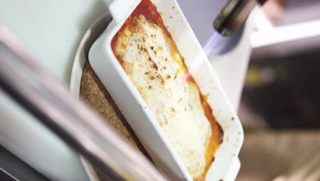 Vertical-slow-motion-panning-shot-of-a-delicious-lasagna-being-flambÃ©ed-by-a-chef-in-an-expensive-gourmet-restaurant-with-a-kitchen-burner-in-a-casserole-dish