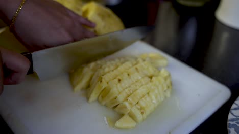 Close-up-of-hands-cutting-yellow-pineapple-on-a-cutting-board