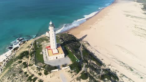 Aerial-Drone-shot-moving-foward-and-passing-by-a-lighthouse-on-a-shore-near-the-beach