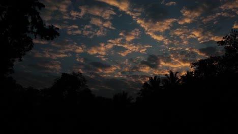 Dark-orange-clouds-moving-across-evening-sky,-dark-silhouettes