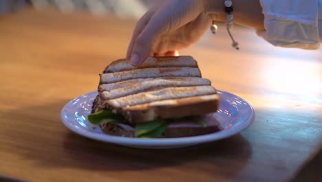 Woman-picking-up-half-sandwich-in-slow-motion-back-light-sunset-restaurant