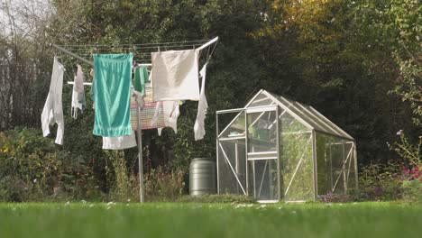 A-Foldable-Outdoor-Clothesline-With-Clean-Clothes-Hangs-To-Dry-Next-To-A-Small-Greenhouse