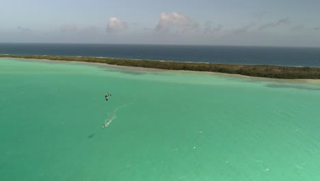 Aerial-shot-pan-left-man-kitesurfing-in-caribbean-paradise-los-roques,-las-salinas-island