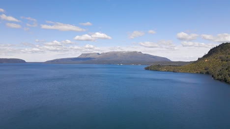 Stunning-granite-mountain-towering-above-the-blue-lake-Tarawera,-New-Zealand