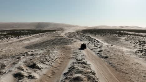 Aerial-tracking-shot-of-quad-bike-driving-on-sandy-dunes-and-Northeastern,Brazil---Desertification-during-sunny-day-in-dry-area