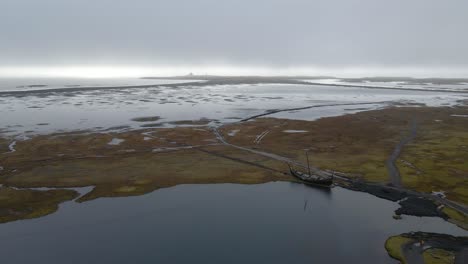 Drone-Flyover-Viking-Barco-Amarrado-En-La-Laguna,-Playa-De-Arena-Negra,-Vestrahorn,-Islandia