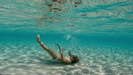 Underwater-scene-of-redhead-little-girl-floating-on-seabed-of-clear-tropical-sea-water-of-exotic-island