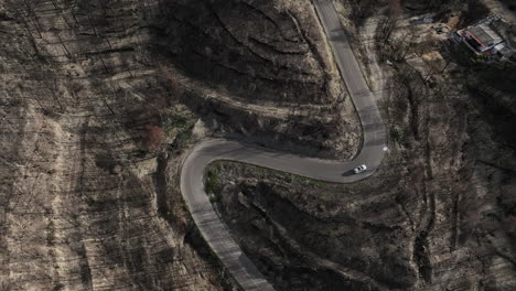 Aerial-shot-of-a-white-car-driving-on-a-sharp-bend-in-a-burned-forest-area