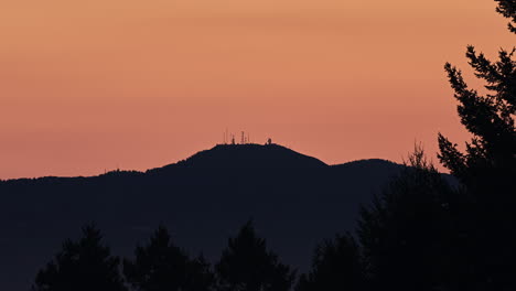 Golden-sunrise-with-a-mountain-in-silhouette-with-antennas-and-microwave-relay-towers-at-the-peak---time-lapse