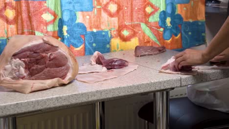 Hands-of-person-slicing-fresh-pork-meat-in-domestic-kitchen,-side-view