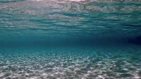Authentic-underwater-scene-of-crystalline-turquoise-tropical-sea-water-with-rippled-surface-and-reflections-on-seabed-with-blue-background