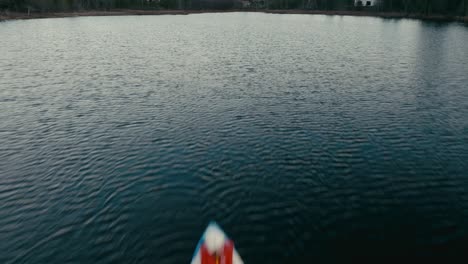 Drone-Fly-Over-A-Person-Kayaking-On-A-Lagoon-With-Waterfront-Cabins